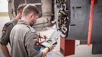 Two soldiers maintaining the engine of a fighter jet.