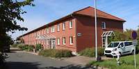 Blick auf ein zweigeschossiges, rot verklinkertes, längliches Gebäude mit Satteldach