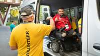 Zwei Personen verabschieden sich voneinander, eine Person sitzt dabei in einem Rollstuhl