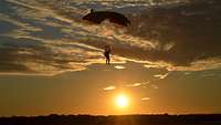 Ein Fallschirmjäger gleitet zu Boden, im Hintergrund geht am Horizont langsam die Sonne unter. 
