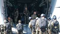 Fallschirmjäger stehen vor der geöffneten Heckrampe eines Flugzeuges, einige sind schon drin.