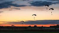 Am Abendhimmel gleiten Fallschirmjäger am Fallschirm Richtung Landezone.