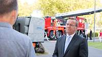 Zwei Männer stehen sich gegenüber, im Hintergrund ein Feuerwehrfahrzeug