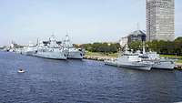 Mehrere Kriegsschiffe festgemacht an einer städtischen Promenade.