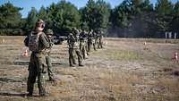 Mehrere Soldaten schießen stehend in einer Reihe im Gelände