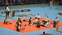 Bei einem Sitzvolleyballspiel spielen viele Sportler in einer großen Halle.