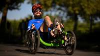 Sportler fährt im im Handbike mit zusammengebissenen Zähnen über eine Straße 