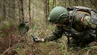 Ein Soldat kniet im Wald auf dem Boden und hält ein