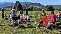 Menschen auf einer Bergwiese vor einem Pfarrer