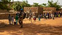 Ein Soldat läuft durch ein Dorf in Mali. Im Hintergrund sind viele malische Kinder.