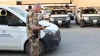 Ein Soldat steht vor einem Auto der Bundeswehr. Im Hintergrund befinden sich weitere Autos.