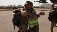 Zwei Soldaten umarmen sich auf einem Flugplatz. Im Hintergrund weitere Soldaten und ein Flugzeug.