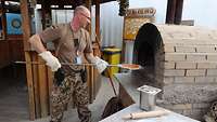 Ein Soldat legt mit einem Pizzaschieber eine Pizza in einen Lehmofen.