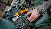 Nahaufnahme: Sprunggepäck mit markant gelbem Griff und der Hand eines Soldaten