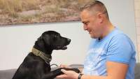 Therapiebegleithund und Patient blicken sich an und geben sich die Pfote bzw. Hand