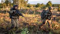 In der Morgensonne stürmen zwei Soldaten durchs niedrigbewachsene Gelände.