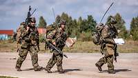Drei Soldaten stürmen über eine Straße.