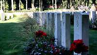 Mehrere Soldaten stehen vor hellgrauen Grabsteinen auf einem Soldatenfriedhof.