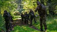 Soldaten laufen in Zweierreihe einen Waldweg entlang und halten ihre Waffen im Anschlag.