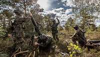 Vier Soldaten schießen auf einer Waldlichtung mit einem Mörser.