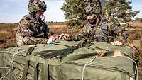 Zwei Soldaten packen die Last, ein sehr großer mit grünem Stoff ummantelter Kasten, aus.