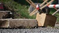 Auf einem Schotterweg mit Betonplatten steht ein brauner Karton mit Schrift.