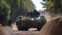Ein Panzer fährt im Wald über einen Schotterweg.