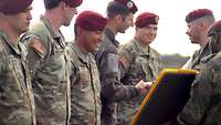 Fünf amerikanische Springer stehen in Reihe, während zwei deutsche Soldaten die Abzeichen verleihen.