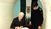 Bundespräsident Richard von Weizäcker trägt sich ins Gästebuch ein. Daneben steht Feldwebel Uwe L. 