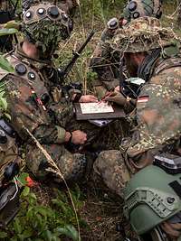 Soldaten sitzen im Gelände, sie sind mit Laserlichtmodulen ausgestattet.