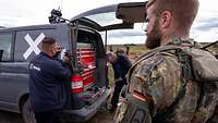 Zwei Techniker stehen neben einem dunkelblauen Kastenwagen, dessen Heckklappe geöffnet ist.