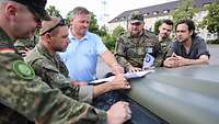 Soldaten und ein Bürgermeister unterhalten sich vor einer Karte, die auf einer Motorhaube liegt