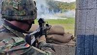 Ein Soldat überwacht eine Wiese. Er steht hinter einer Barrikade und hält eine Waffe