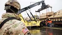 Operation Atlantic Resolve Ein amerikanischer Soldat steht vor einem Kran, der Kettenfahrzeuge entlädt.