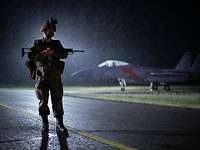 Übung Air Defender 23 Ein Soldat eine steht bei Nacht vor einem Flugzeug. Er trägt eine Waffe.