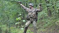 Ein Soldat geht seitlich auf einem Seil über einen Bach und hält sich an einem zweiten fest.