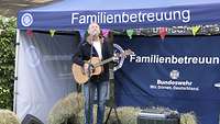 Ein Gitarrist steht vor einem Pavillon und singt.