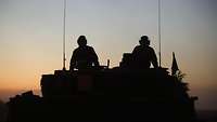 Die Silhouette von zwei Soldaten auf dem Turm eines Kampfpanzers.