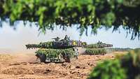Zwei Kampfpanzer fahren auf einem Sandtrack.