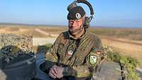 Ein Soldat mit einem Headset auf dem Kopf schaut aus der Luke eines Kampfpanzers.
