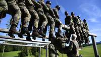 Viele Soldaten sitzen auf einem Stamm in einigen Metern Höhe und versuchen das Hindernis gemeinsam zu überwinden. 