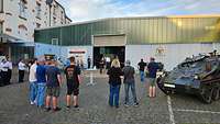 Group of visitors A group of people is standing in front of an exhibition hall. A tank is standing at the side.
