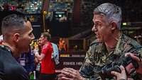 Ein Sportler und ein Soldat schütteln sich die Hand. Sie sprechen angeregt miteinander. 