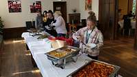 An einem Buffet stehen Personen und nehmen sich etwas zu essen.