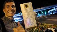 Ein Mann zeigt vor dem Haupttor des BMVg in Bonn auf der Hardthöhe mit erhobenem Daumen eine 1