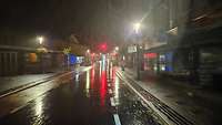 Eine Straße in Waldbröl bei Nacht bei heftigem Regen, Lichter spiegeln sich auf der nassen Fahrbahn