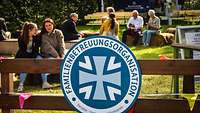 Mehrere Menschen sitzen auf Bänken auf einer Wiese zusammen und unterhalten sich. 