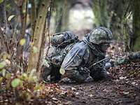 Grundausbildung Ein Soldat kriecht durch das Gelände. Weitere Soldaten unscharf im Hintergrund.