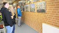 Ein Mann in einer blauen Jacke schaut sich Bilder die an einer Wand hängen an. 