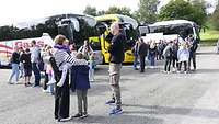 Mehrere Menschen stehen vor drei Reisebussen.